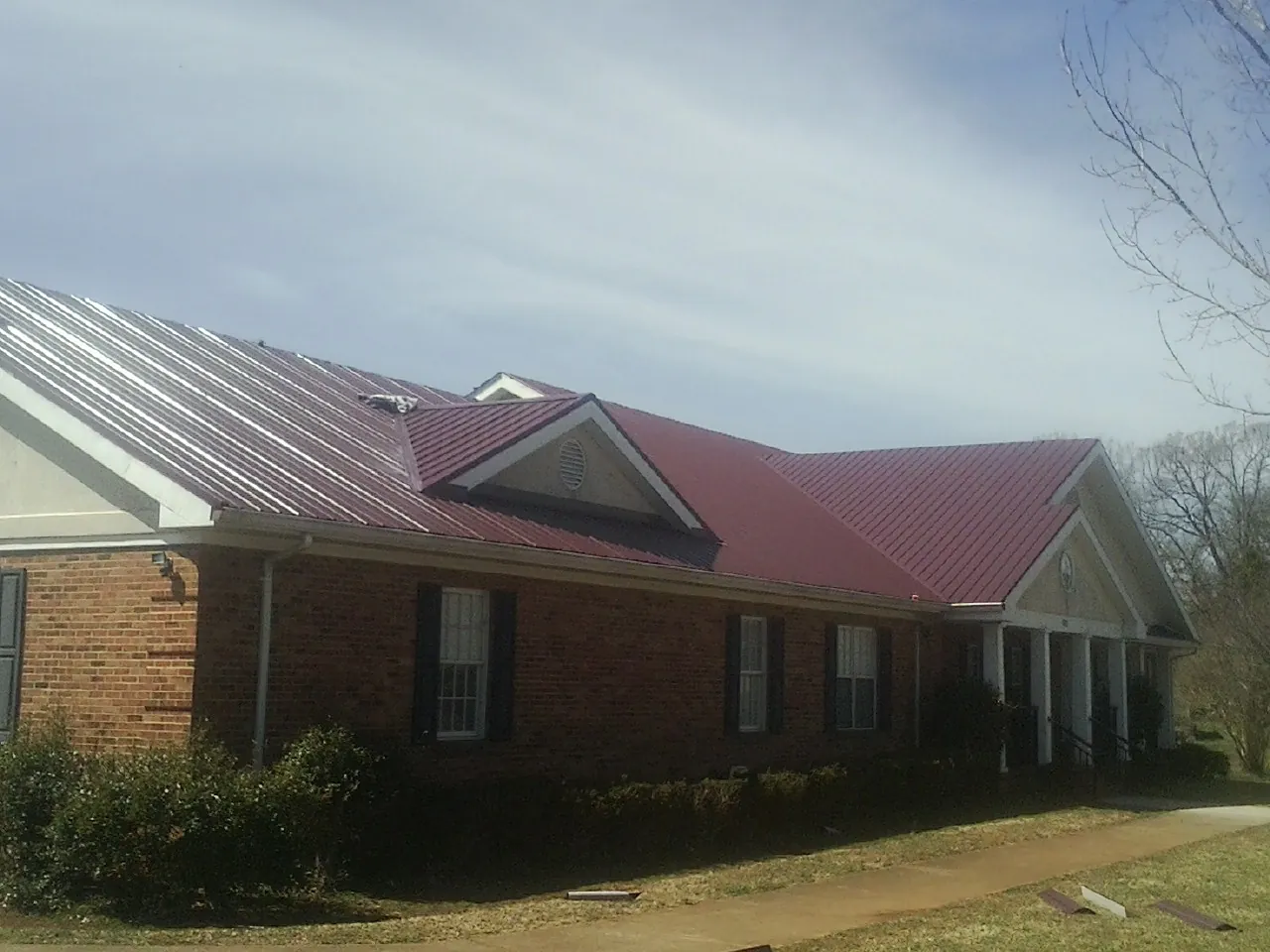 Red metal roof with gabled entries on a long brick building, from a Hail Damage Roof Repair job in Manvel