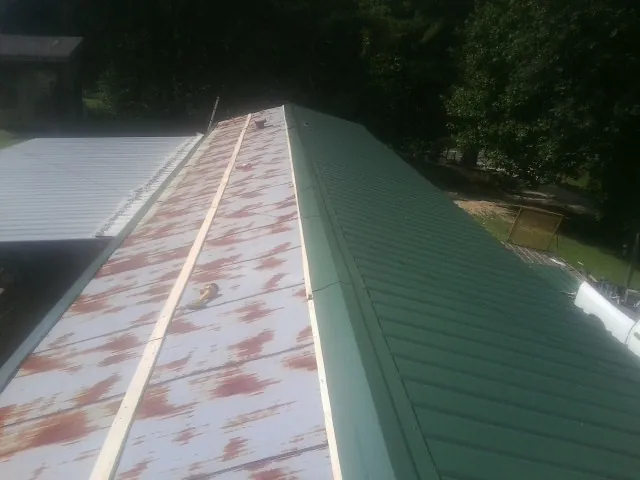 Old rusted panels beside newly installed green metal roofing — Wind Damage Roof Repair by Roofing Brothers in Manvel