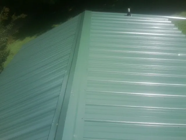 New green metal panels meeting at the ridge of a roof — Flat Roof Repair work by our crew in Manvel